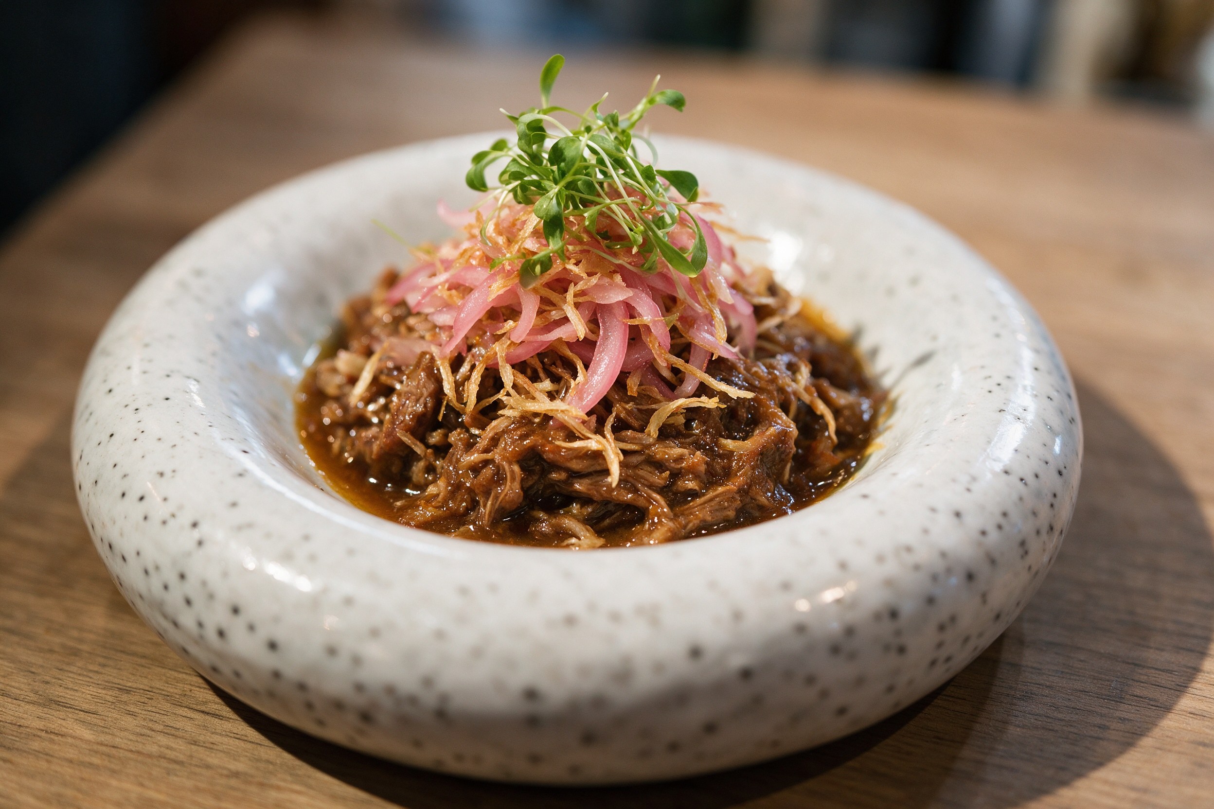 Tapa de carne melosa con cebolla morada y brotes en bol cerámico moteado
